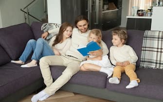 Happy family with children reading book together sitting on sofa