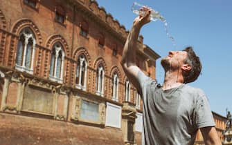 Mid-adult man standing in the Piazza del Nettuno or Piazza Maggiore by the Pallzzo d'Accursio and pouring cold water on his face to cool down.