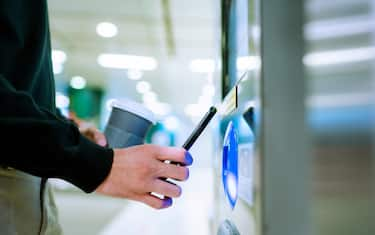 Close up of a young Asian man using contactless payment via smartphone to pay for her shopping at self-checkout kiosk in subway