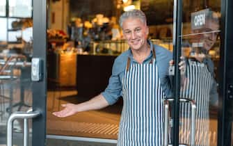 Business owner at the door of a cafe welcoming customers and looking very happy
