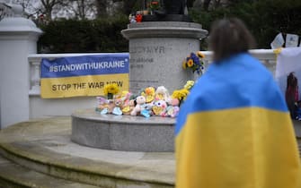 A woman wrapped in a Ukraine national flag stands in front of Statue of Saint Volodymyr in central London, during the National one minutes silence to mark one year since the invasion of Ukraine by Russia, on February 24, 2023. (Photo by Daniel LEAL / AFP) (Photo by DANIEL LEAL/AFP via Getty Images)