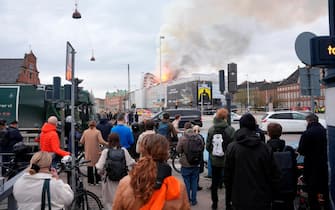epa11281332 Locals look on as a fire burns the old Stock Exchange (Boersen) in Copenhagen, Denmark, 16 April 2024. A violent fire broke out in the building which is under renovation on the morning of 16 April. The building was erected in the 1620s as a commercial building by King Christian IV and is located next to the Danish parliament.  EPA/Ida Marie Odgaard DENMARK OUT