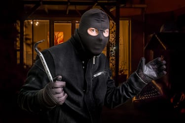 Masked thief in balaclava with crowbar wants to rob a house at night