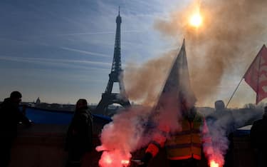 TOPSHOT - A members of the SUD labour union holds flares during a demonstration on the Parvis du Trocadero, across the Seine river from the Eiffel Tower, during a cross-sector labour union protest against France's controversial pension reform bill, in Paris, on February 9, 2023. - The planned reforms include hiking the retirement age from 62 to 64 and increasing the number of years people must make contributions for a full pension. (Photo by Alain JOCARD / AFP) (Photo by ALAIN JOCARD/AFP via Getty Images)
