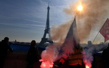 TOPSHOT - A members of the SUD labour union holds flares during a demonstration on the Parvis du Trocadero, across the Seine river from the Eiffel Tower, during a cross-sector labour union protest against France's controversial pension reform bill, in Paris, on February 9, 2023. - The planned reforms include hiking the retirement age from 62 to 64 and increasing the number of years people must make contributions for a full pension. (Photo by Alain JOCARD / AFP) (Photo by ALAIN JOCARD/AFP via Getty Images)