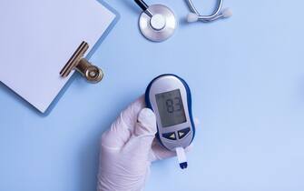 Glove hand Of Doctor with glucose meter on blue background top view.