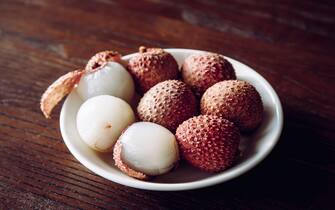 Tropical fruit Lychee known as Litchi chinensis berries on plate, dark brown wood background, dramatic light, studio shot.