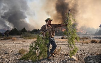 A local man holds a pine tree branch to beat down the approaching wildfires burn in the background, near the village of Vati, just north of the coastal town of Gennadi, in the southern part of the Greek island of Rhodes on July 25, 2023. Some 30,000 people fled the flames on Rhodes at the weekend, the country's largest-ever wildfire evacuation as the prime minister warned that the heat-battered nation was "at war" with several wildfires and spoke of three difficult days ahead.. (Photo by Angelos TZORTZINIS / AFP) (Photo by ANGELOS TZORTZINIS/AFP via Getty Images)