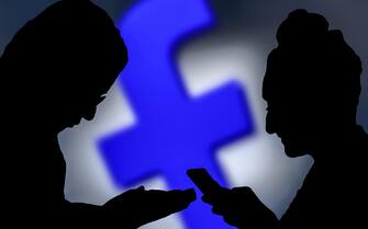 Silhouettes of a couple of people using the Facebook app on smartphones.