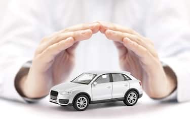 Car insurance. Small silver toy car covered by hands