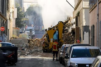Firefighters stand next to a truck moving rubbles where a building collapsed in Marseille, southern France, on April 9, 2023. - "We have to be prepared to have victims," the mayor of Marseille warned on April 9, 2023 after a four-storey apartment building collapsed in the centre of France's second city, injuring five people, according to a provisional report. (Photo by NICOLAS TUCAT / AFP) (Photo by NICOLAS TUCAT/AFP via Getty Images)