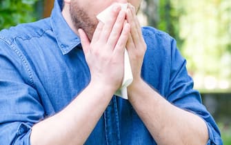 Man in public park blowing his nose and suffering from pollen allergy.