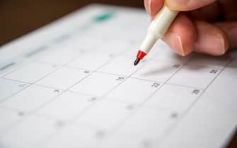 The hand of a man holding a pen in his hand and recording his schedule on a desk calendar