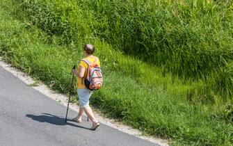 Elderly woman Nordic walking on country road, active aging