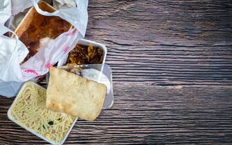 Chinese takeaway food selection in plastic bag. Bami, babi pangang, crispy shredded beef, sweet and sour chicken, krupuk top view on wooden table copy space. Food delivery