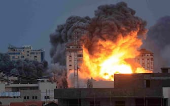 EDITORS NOTE: Graphic content / People standing on a rooftop watch as a ball of fire and smoke rises above a building in Gaza City on October 7, 2023 during an Israeli air strike. At least 70 people were reported killed in Israel, while Gaza authorities released a death toll of 198 in the bloodiest escalation in the wider conflict since May 2021, with hundreds more wounded on both sides. (Photo by MAHMUD HAMS / AFP)