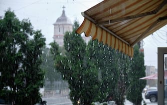 Store front awning dripping during heavy rain storm.  Street view with church in background