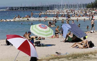epa10739914 People sit on the Baby plage on the bank of the Geneva lake, in Geneva, Switzerland, 11 July 2023. A heatwave is affecting Geneva with temperatures reaching over 38 degrees Celsius.  EPA/SALVATORE DI NOLFI