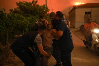 epa10812679 Volunteers assist an elderly man during a wildfire in Avantas village, near the city of Alexandroupolis, Thrace, northern Greece, 21 August 2023. The wildfire that broke out early on 19 August in a forest in the Melia area of Alexandroupolis has spread rapidly due to the strong winds blowing in the area and is raging uncontrolled. The major wildfire in Alexandroupolis continues with unabated intensity for the third consecutive day. According to the Fire Department, the fire is difficult to be contained due to the strong winds in the area.  EPA/DIMITRIS ALEXOUDIS
