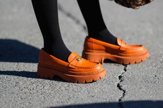 NEW YORK, NEW YORK - FEBRUARY 14: A guest wears black tights, orange shiny leather platform loafers from Coach, outside the Coach show, during New York Fashion Week, on February 14, 2022 in New York City. (Photo by Edward Berthelot/Getty Images)