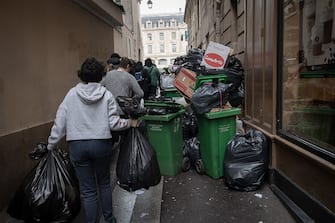 People carry waste bags past waste that has been piling up on the pavement as waste collectors are on strike since March 6 against the French government's proposed pensions reform, in Paris on March 13, 2023. (Photo by ALAIN JOCARD / AFP) (Photo by ALAIN JOCARD/AFP via Getty Images)