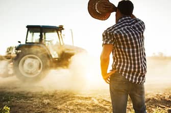 Farmer covers face from sun in a hot day at the fields as tractor passes by. More files of this series and models on port.