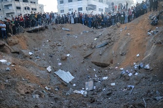 TOPSHOT - Palestinians stand on the edge of a crater after an Israeli strike in Rafah in the southern Gaza Strip on December 3, 2023, amid continuing battles between Israel and the militant group Hamas. Israel carried out deadly bombardments in Gaza on December 3 as international calls mounted for greater protection of civilians and the renewal of an expired truce with Palestinian militant group Hamas. (Photo by SAID KHATIB / AFP)