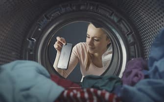 Disappointed woman finding her phone in the washing machine, the phone is damaged and dripping water