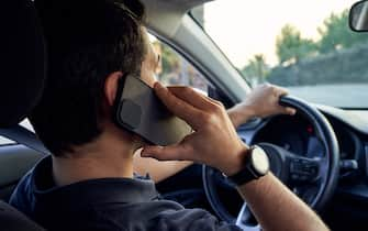 Rear view of a young unrecognizable Hispanic man talking on a smartphone while driving his car. Concept of driving and road safety.