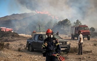 A firefighter wearing a mask looks on as wildfires burn the hill side forests near the village of Vati, just north of the coastal town of Gennadi, in the southern part of the Greek island of Rhodes on July 25, 2023. Some 30,000 people fled the flames on Rhodes at the weekend, the country's largest-ever wildfire evacuation as the prime minister warned that the heat-battered nation was "at war" with several wildfires and spoke of three difficult days ahead.. (Photo by Spyros BAKALIS / AFP) (Photo by SPYROS BAKALIS/AFP via Getty Images)