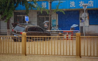 epa10779179 People walk next to a damaged by flood car during a downpour in Mentougou District, west of Beijing, China, 01 August 2023. Heavy rains brought by Typhoon Doksuri caused floods in northern China and left two dead and thousands being evacuated as Beijing experienced its heaviest rainfall of the year.  EPA/MARK R. CRISTINO
