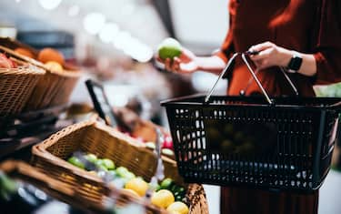 Cropped shot, mid-section of young Asian woman carrying a shopping basket, grocery shopping for fresh organic fruits and vegetables in supermarket, she is choosing green apple along the produce aisle. Healthy eating lifestyle. Zero waste concept