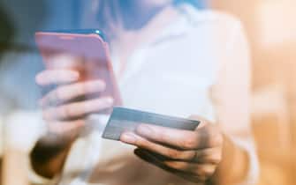 Young woman shopping online with smartphone and credit card on hand.