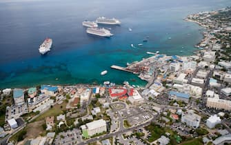 Cruise ships anchor in waters offshore of Georgetown Harbor in Grand Cayman.  The existence of shallow coral reefs prohibit the ships from entering the harbor.  Tenders take passengers to and from the shore. Aerial view