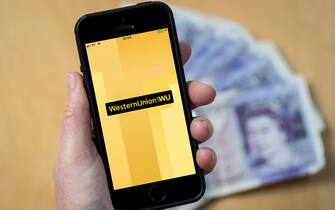 A woman using the Western Union app on a mobile phone. (Editorial Use Only)