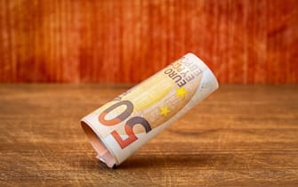 Roll of fifty euro banknotes falling on the wooden background