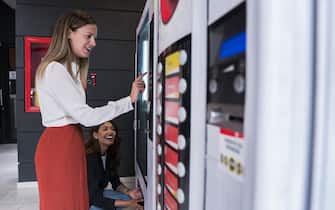 Ethnic Latin women between 25-35 years old co-workers are at break from work using the coworking office vending machine