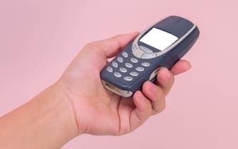 Close up hand holding mobile phone Nokia 3310 isolated on pink background. Female hand holding old used phone Nokia 3310.