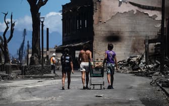epa10795999 Residents push a kart amid the ruins left by a wild fire that swept through the city up to the shore and port in Lahaina, Hawaii, USA, 11 August 2023. At least 67 people were killed in the wildfires burning in Maui, which is considered the largest natural disaster in Hawaii's state history.  EPA/ETIENNE LAURENT