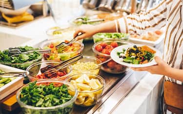 Woman choosing food for breakfast at hotel restaurant. Woman taking food from a buffet line.