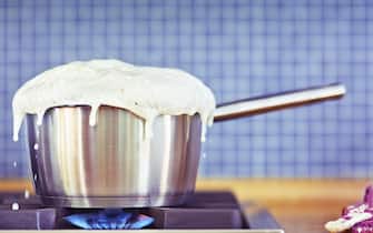 Milk boiling over in pan on gas stove.