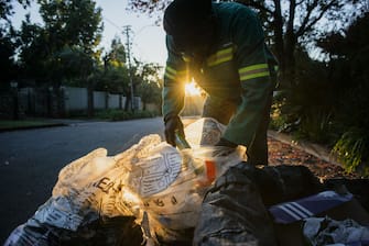 A waste-picker sorts through a sack of domestic trash as the sun rises in a wealthy suburb of Johannesburg, South Africa, on Friday, May 3, 2019. A legacy of apartheid, inequality remains so ingrained the ruling African National Congress hasnt been able to narrow the wealth gap since taking power 25 years ago. Photographer: Waldo Swiegers/Bloomberg via Getty Images
