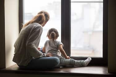 Rear view at kid daughter and mother sitting on sill