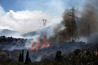 epa10751571 A fire burns next to high voltage electricity pylons at Kouvaras area in Attica, Greece, 17 July 2023. Firefighting forces are battling a blaze that broke out in the Kouvaras area in Attica, while a warning was sent via the emergency number 112 to evacuate several settlements in southeast Attica. A force of 55 firefighters and 20 fire engines, two units on foot and 31 Romanian firefighters with five water tankers have been deployed to put out the fire, assisted by six fire-fighting aircraft and four helicopters from the air.  EPA/YANNIS KOLESIDIS