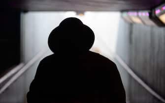 silhouette of man in trilby and overcoat, in an underpass London, UK