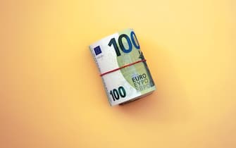 Roll of euro banknotes. 100 euro with red rubber band on yellow background