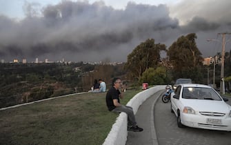 epa11122248 People sit outdoors as smoke from a fire that started in the Penuelas Lake natural reserve covers the sky over Vina del Mar, Chile, 02 February 2024. The first major forest fire of the summer threatens the coastal cities of Valparaiso and Vina del Mar, forcing the evacuation of several inland communes, with smoke reaching the beaches of Concon, Quintero and Maitencillo, almost a hundred kilometers from the fire epicenter.  EPA/ADRIANA THOMASA