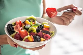 A woman breakfasts a fruit salad high in vitamins and fiber.