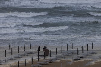 CERVIA, ITALY - SEPTEMBER 17: Two men bring deck chairs and parasols to safety from a flooded beach near Cervia in the Italian region of Emilia Romagna on September 17, 2022 in Cervia, Italy. After a summer of extreme heat and drought, Italy is hit by a wave of storms. Several people died and some others are missing after a rainstorm dumped more than a foot of water on a coastal area of central Italy. (Photo by Jan Hetfleisch/Getty Images)