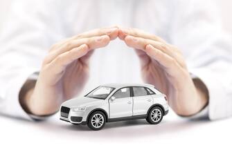 Car insurance. Small silver toy car covered by hands